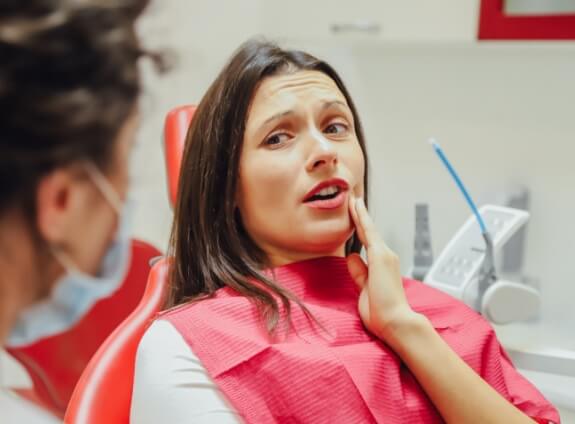 Woman in dental chair holding her cheek in pain